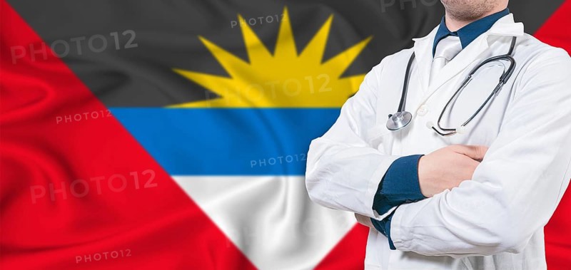 Antigua and Barbuda healthcare concept. Male doctor on Antigua and Barbuda flag. Doctor with crossed arms on Antigua and Barbuda flag