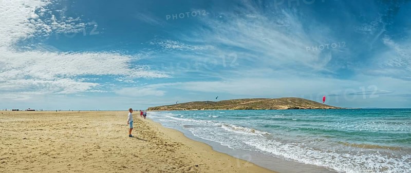Wide sandy beach of Prasonisi with gentle waves, distant peninsula and kite surfers under a blue sky, Prasonisi, Rhodes Island, Greece