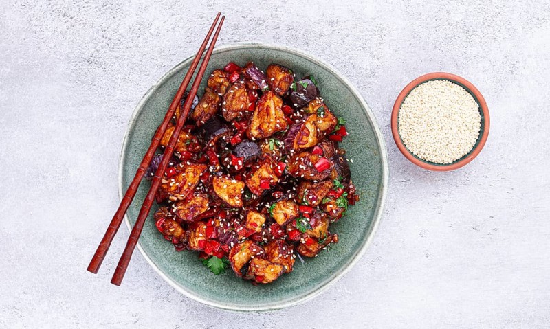 Fried eggplant, Chinese style, in sweet and sour sauce, with pepper and sesame seeds, in a green bowl