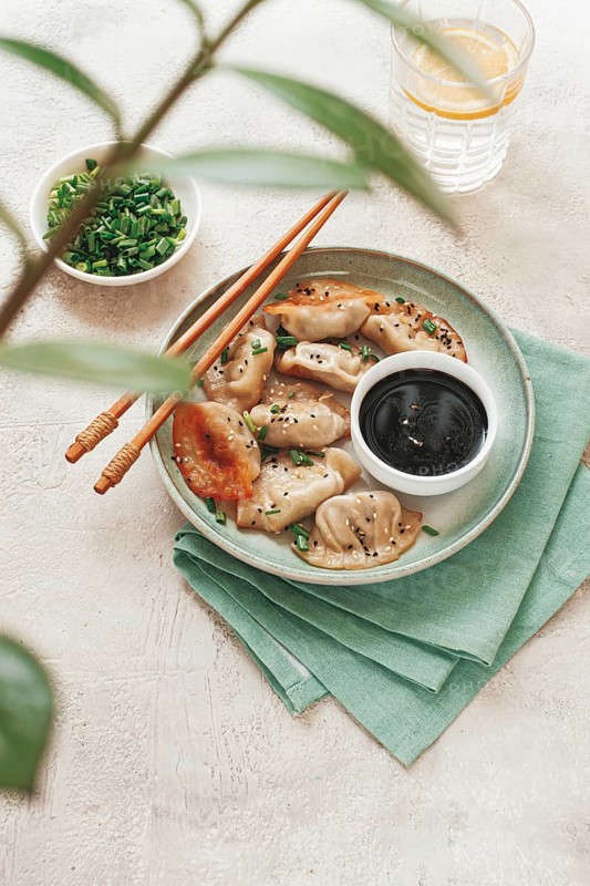 Gyoza Japanese dumplings, fried, with sauce, green onion, and sesame seeds, natural color, light background