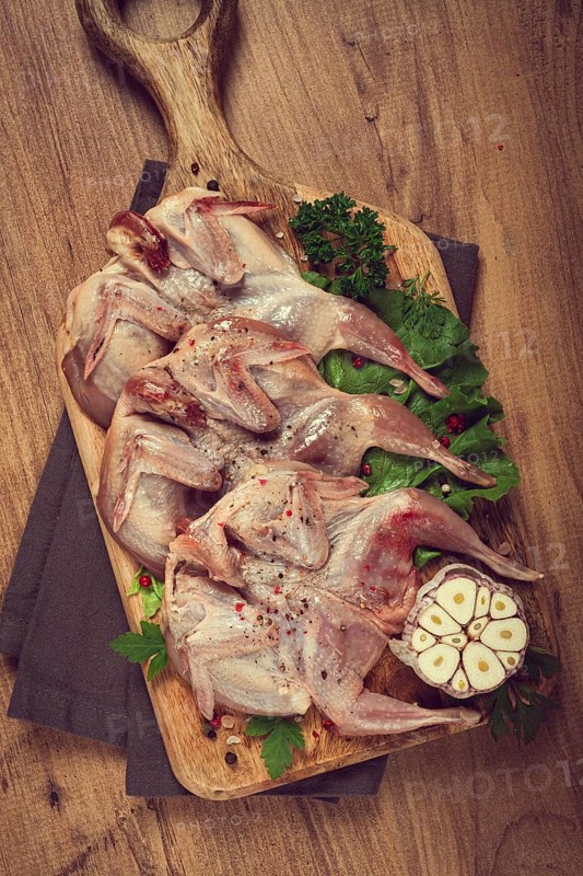 Raw quail meat, on a cutting board, with spices and herbs, top view