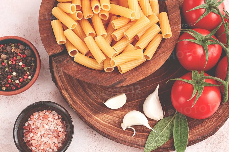 Pasta ingredients spread out, on a wooden surface, with tomatoes and spices, ready to cook, there are no people