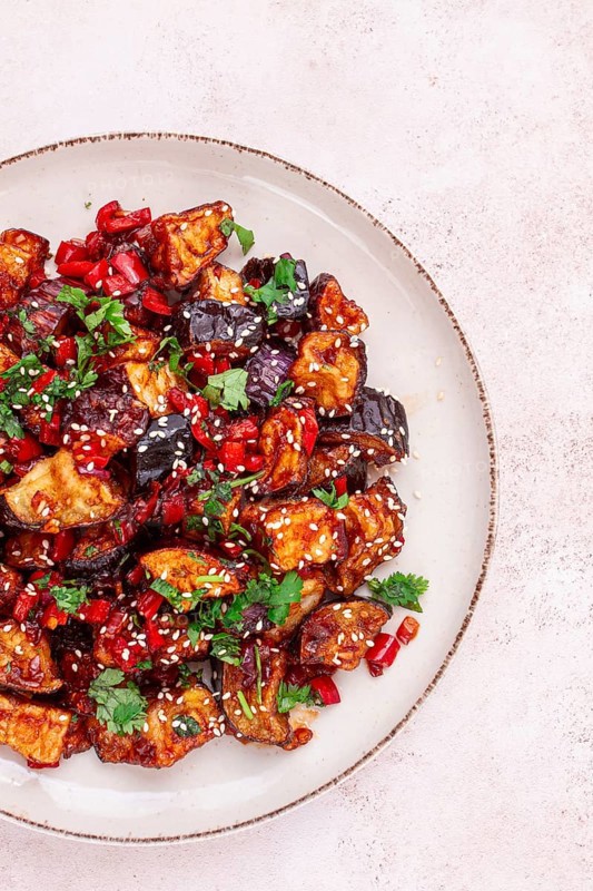Fried eggplant, Chinese style, in sweet and sour sauce, with pepper and sesame seeds. on a white plate