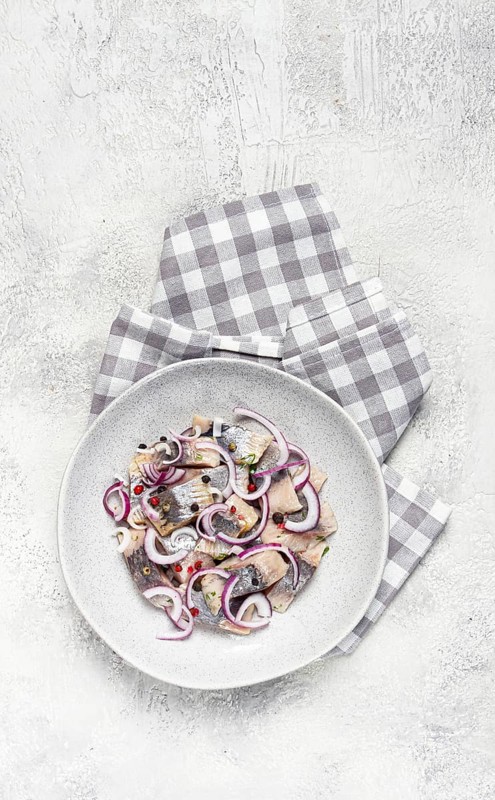 Salted herring, with spices and red onion, sliced fillet, on a plate, top view