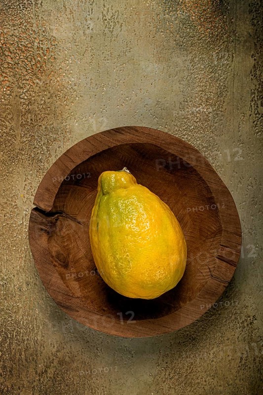 A vibrant yellow papaya is positioned in a rustic wooden bowl, resting on a textured surface that complements its colors, illuminated by gentle, soft light