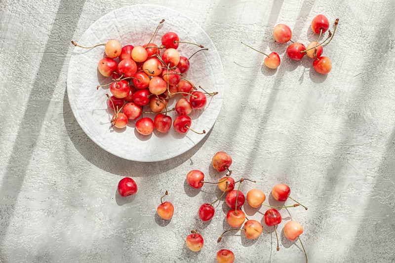 Yellow cherries on a white platter, scattered on the table, natural light, top view