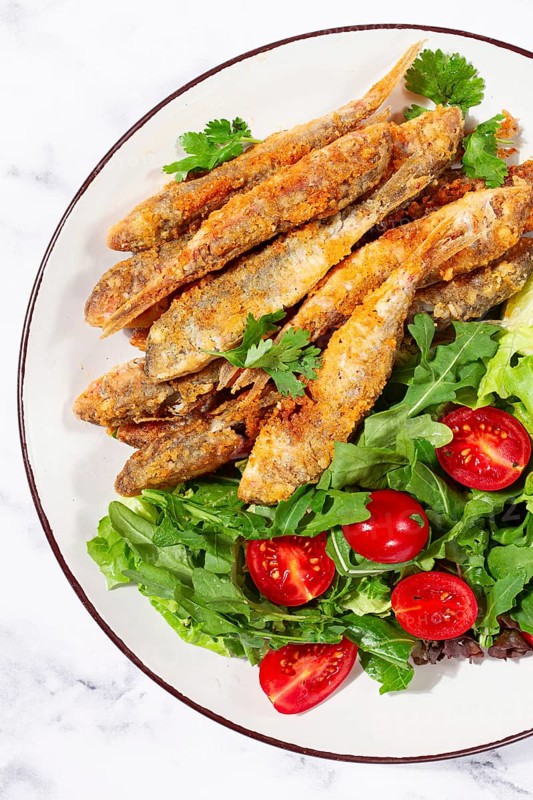 Fried crispy mullet fish, with fresh salad, on a plate with lime, no people