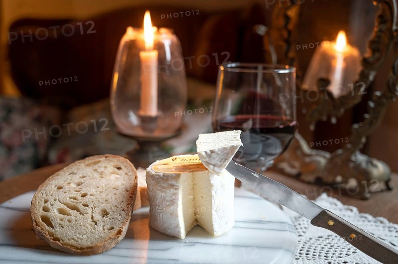 Chaource cheese presented sliced with bread and red wine in warm candlelight, typical of the Champagne region, impresses with its fluffy white mould rind, creamy, mild core and fine, creamy flavours - an artisan cheese with a centuries-old tradition and AOP label, produced by the Fromagerie de Mussy, Chaource, Aube department, Grand Est region, France