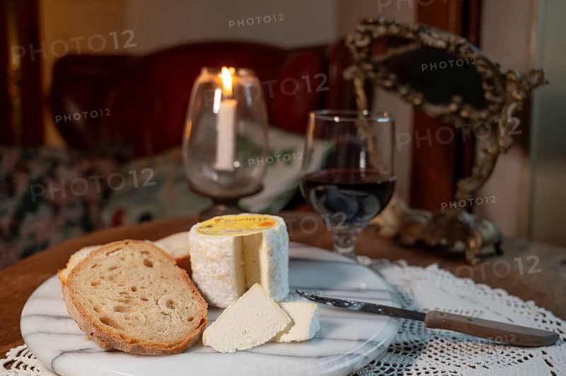 Chaource cheese presented sliced with bread and red wine in warm candlelight, typical of the Champagne region, impresses with its fluffy white mould rind, creamy, mild core and fine, creamy flavours - an artisan cheese with a centuries-old tradition and AOP label, produced by the Fromagerie de Mussy, Chaource, Aube department, Grand Est region, France
