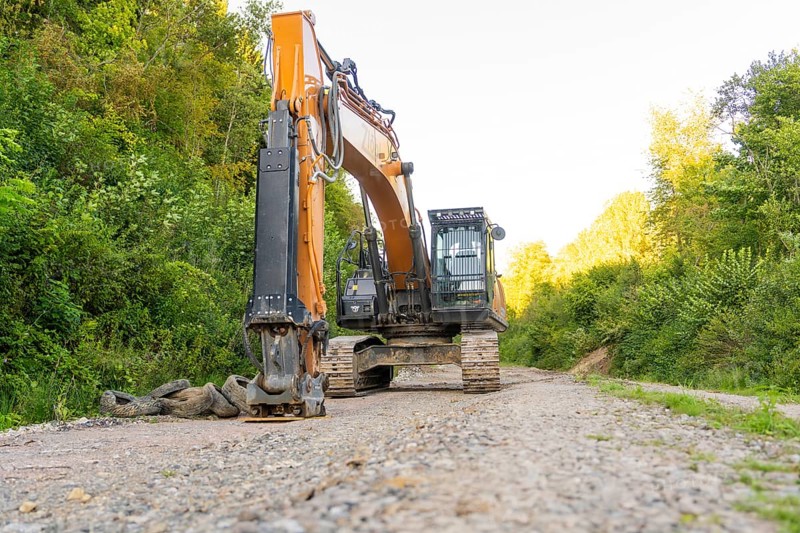 A large excavator stands on a dirt road in a wooded area, Hermann Hessebahn construction site, Calw, Germany
