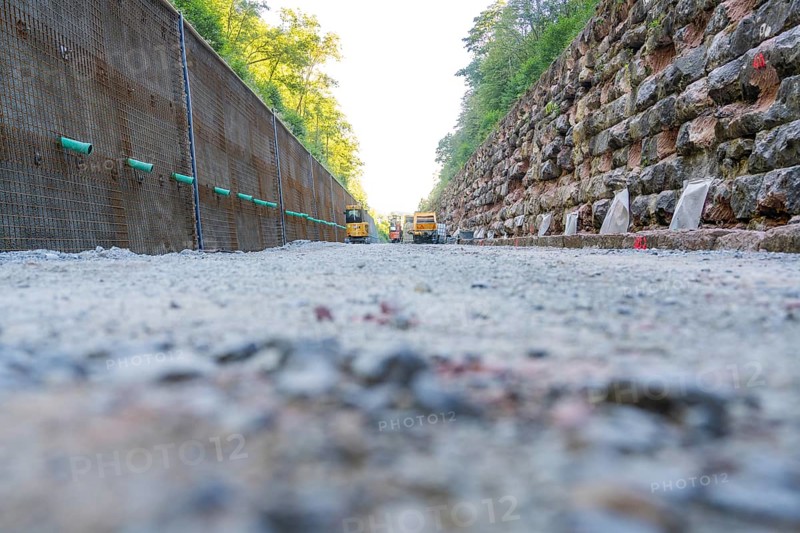 Gravel path between a concrete and a stone wall with construction machinery in the background, Hermann Hessebahn construction site, Calw, Germany
