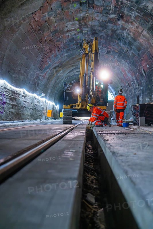 Construction workers in a tunnel carry out work with a large machine. Neon lights illuminate the scene, construction of the Hermann Hesse railway, Calw, Black Forest, Germany