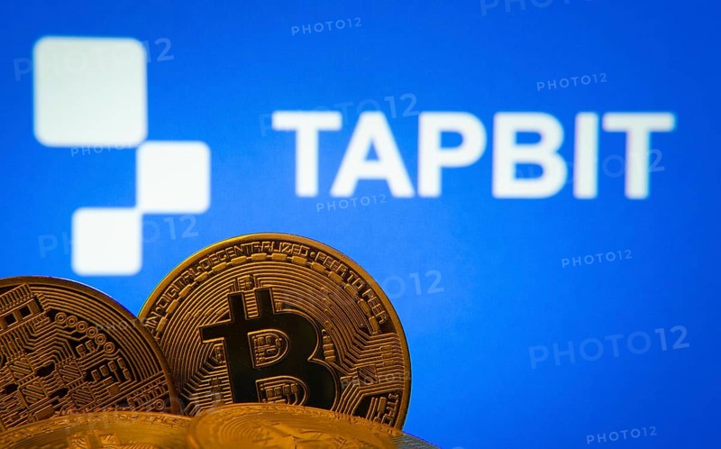 Dhaka, Bangladesh- 20 Sep 2025: Close-up of Bitcoin coins with thex Tapbit logo visible on a screen in the background