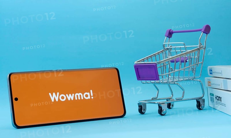 Dhaka, Bangladesh- 03 July 2025: Smartphone with wowma logo next to a small shopping cart and boxes against a blue background