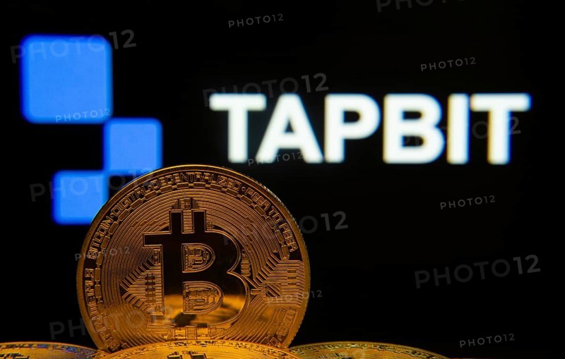 Dhaka, Bangladesh- 20 Sep 2025: Close-up of Bitcoin coins with thex Tapbit logo visible on a screen in the background