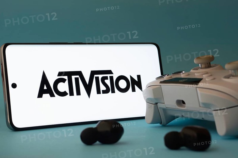Dhaka, Bangladesh- 23 Sep 2025: A smartphone with a Activision icon next to a controller and earbuds on a blue surface