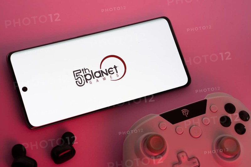 Dhaka, Bangladesh- 23 Sep 2025: Smartphone with 5th planet games logo, game controller, and earbuds on a pink background