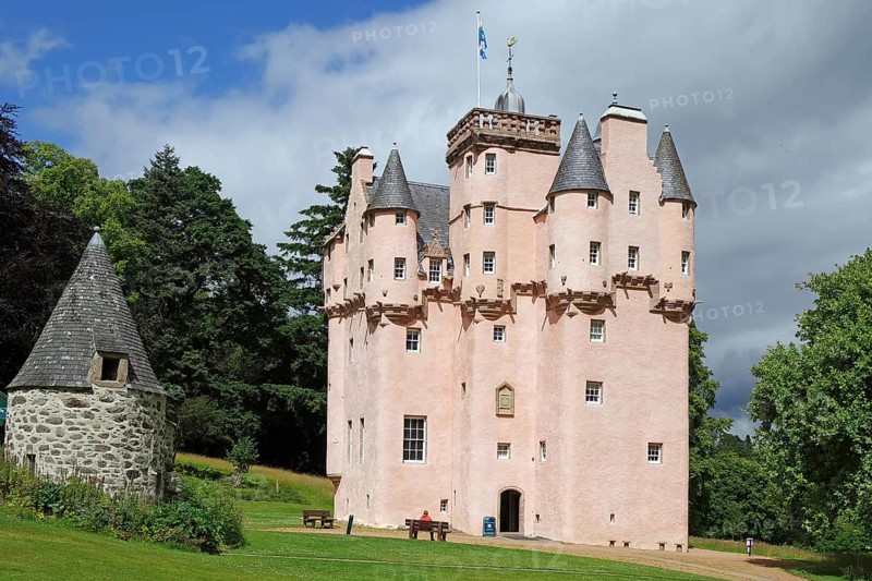 Pink castle with turrets and banner in a meadow under a cloudy sky, Craigievar Castle, Aberdeenshire, Scotland, United Kingdom