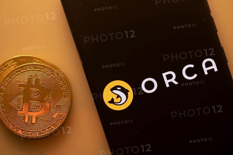 A Bitcoin and Orca logo on a black screen with a yellow circle