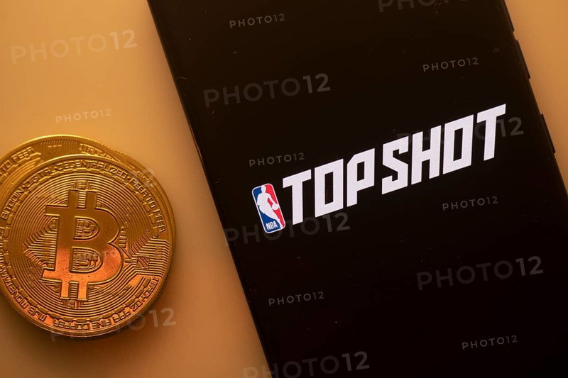 A Bitcoin and Top Shot logo on a black screen representing cryptocurrency