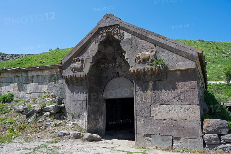 An old stone building with reliefs and a large entrance surrounded by green hills, Selim Caravanserai, Orbelian Caravanserai, Vayots Dzor Province, Armenia