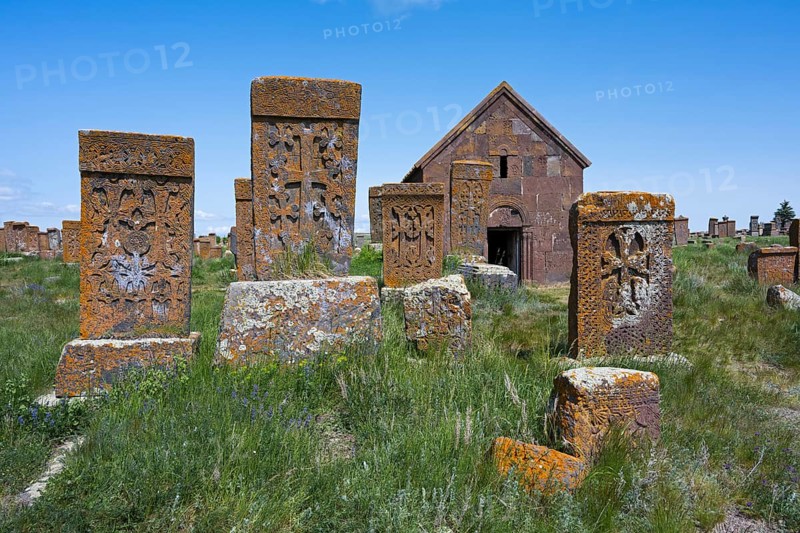 Old gravestones and a chapel in a green cemetery under a bright blue sky, cross stones, the world's largest field of Khachkars, Noratus cemetery, Noradus, Gegharkunik province, Armenia