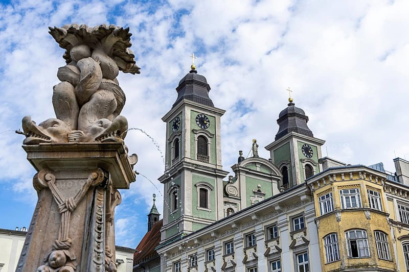 Baroque sculpture next to a building with towers and cloudy sky, Old Cathedral Ignatius Church Old Town Linz Upper Austria Austria