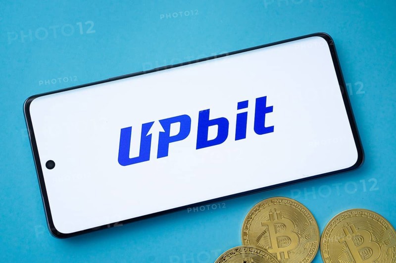 Dhaka, Bangladesh- 19 Sep 2025: Upbit logo on smartphone screen near Bitcoin coin and QR code on blue background