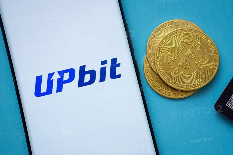 Dhaka, Bangladesh- 26 Aug 2025: Upbit logo on smartphone screen near Bitcoin coin and QR code on blue background