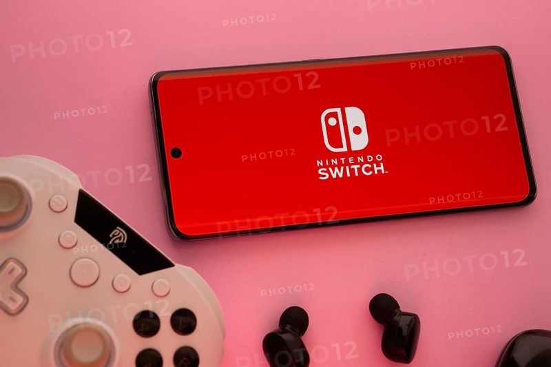 Dhaka, Bangladesh- 15 July 2025: Smartphone with nintendo switch logo, game controller, and earbuds on a pink background