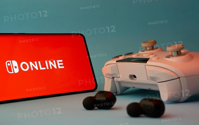 Dhaka, Bangladesh- 15 July 2025: A smartphone with a nintendo online icon next to a controller and earbuds on a blue surface