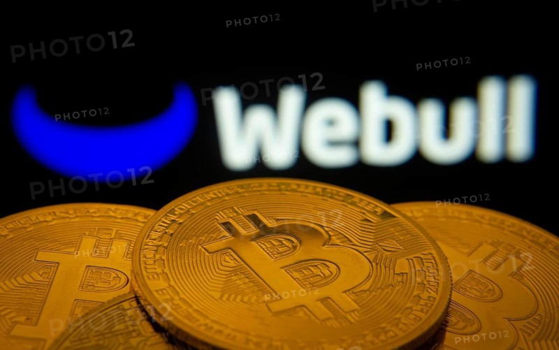 Dhaka, Bangladesh- 27 July 2025: Close-up of Bitcoin coins with the webull logo visible on a screen in the background