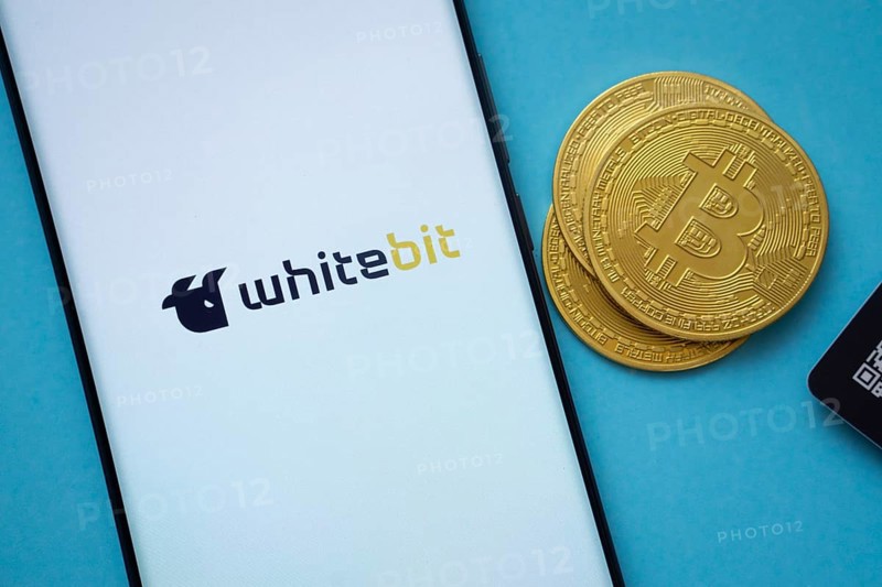 Dhaka, Bangladesh- 03 Sep 2025: Whitebit logo on smartphone screen near Bitcoin coin and QR code on blue background