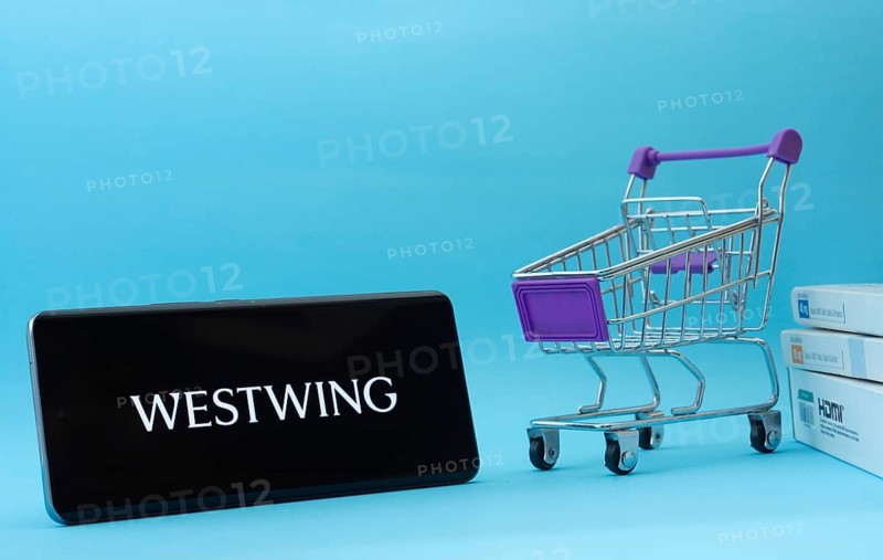Dhaka, Bangladesh- 03 July 2025: Smartphone with Westwing logo next to a small shopping cart and boxes against a blue background