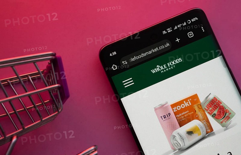 Dhaka, Bangladesh- 23 June 2025: A smartphone displaying the Whole Foods Market website with a shopping cart is shown on a vibrant background