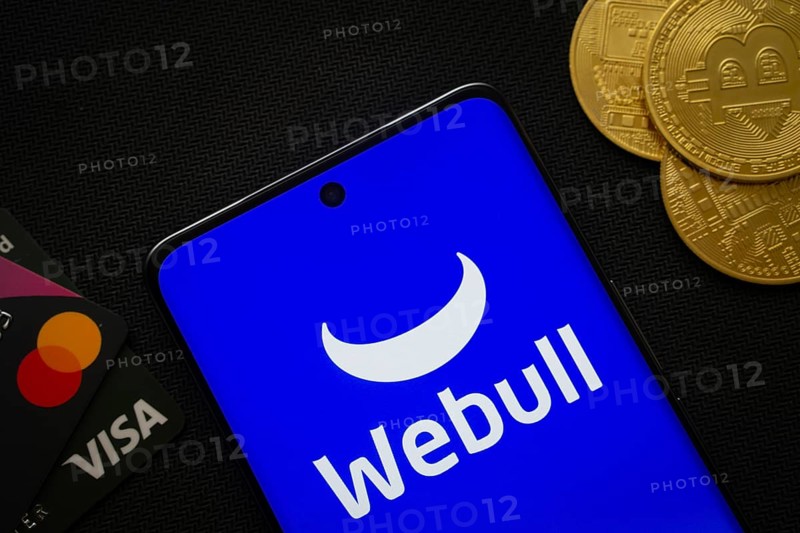 Dhaka, Bangladesh- 26 Aug 2025: Smartphone displaying webull logo surrounded by Bitcoin coins and payment cards