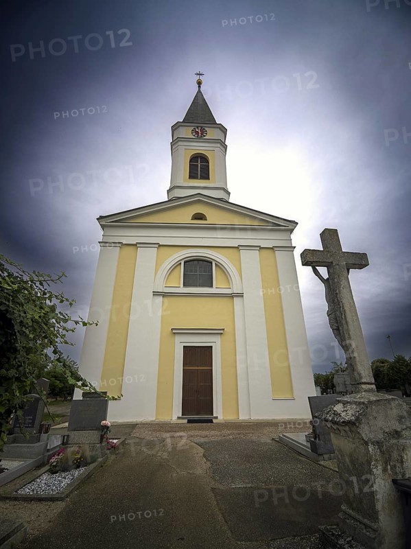 Yellow church with tower and cross in a cemetery under a cloudy sky, Kammersdorf Hollabrunn Weinviertel Lower Austria Austria