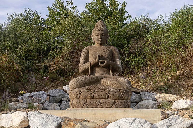 Sitting Buddha statue surrounded by stones and vegetation, Stupa am Wagram Grafenwörth Weinviertel Lower Austria Austria