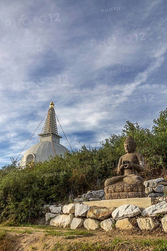 Buddha statue sitting on stones with a pagoda in the background and cloudy sky, Stupa am Wagram Grafenwörth Weinviertel Lower Austria Austria