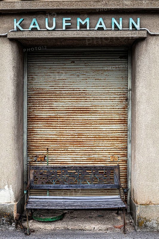 In front of a closed merchant's shop with a rusty Tor tor stands an old bench that suggests a bygone era, Weinviertel Lower Austria Austria