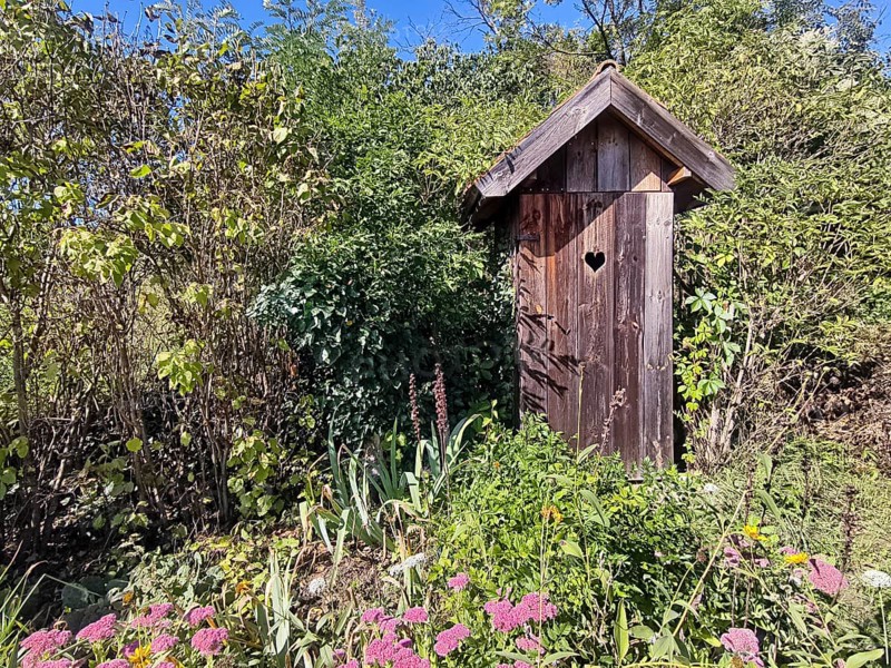 A small wooden house in the garden with a heart symbol on the door Outhouse, surrounded by plants and flowers, Weinviertel Lower Austria Austria