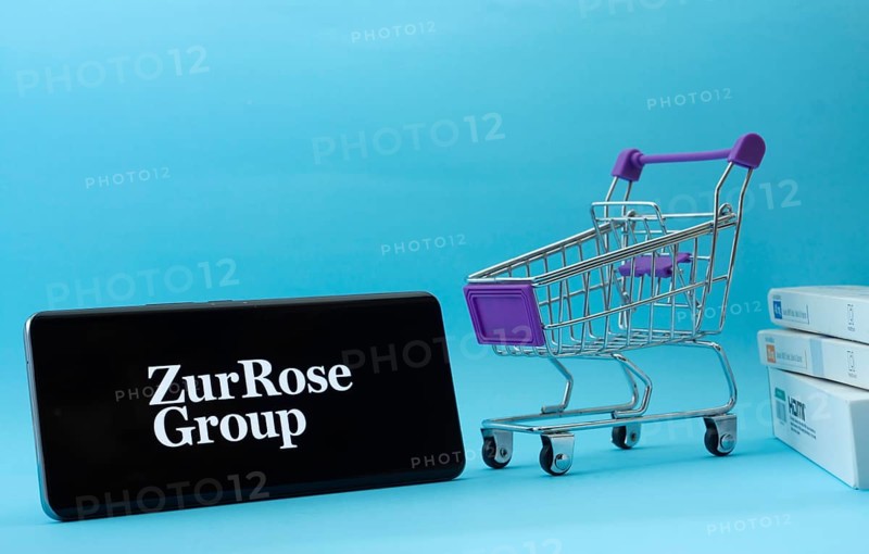 Dhaka, Bangladesh- 03 July 2025: Smartphone with Zur Rose Group logo next to a small shopping cart and boxes against a blue background