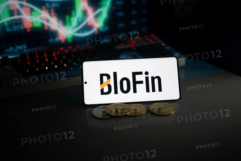 BloFin display with coins in front of an active stock chart under neon lighting