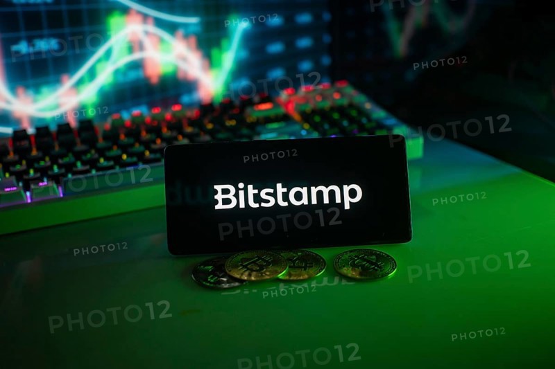 Bitstamp logo in a dim setting with coins and a vivid chart