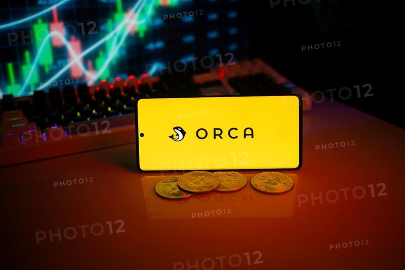 Yellow Orca logo on phone with coins and market screen, indicating crypto trading