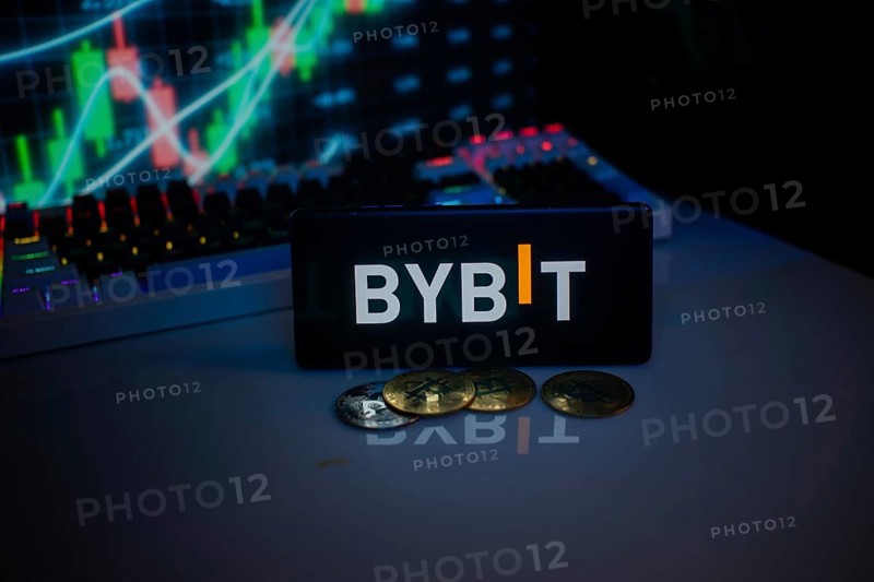 BYBIT logo on smartphone, accompanied by coins and stock chart, conveying trading theme