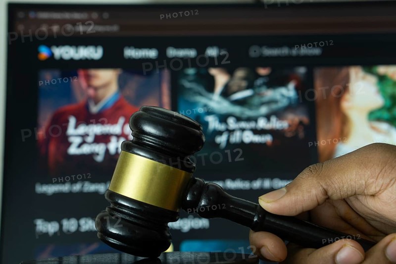 Dhaka, Bangladesh- 20 June 2025: A hand holds a gavel in front of a computer screen displaying YOUKU website