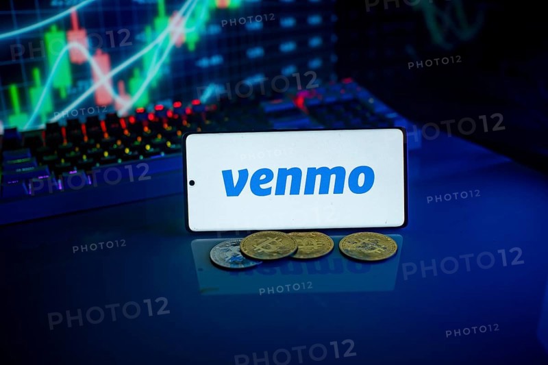 Phone displaying Venmo logo with coins and a backlit keyboard, signifying digital payments and finance
