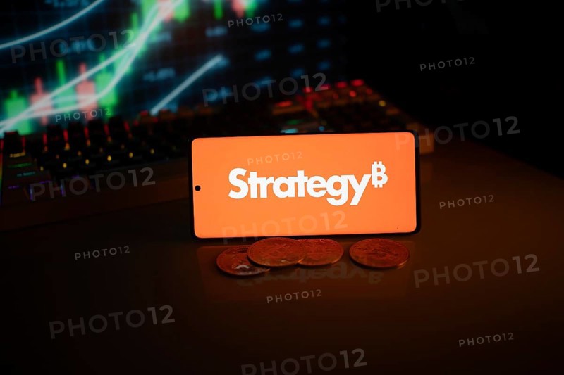 Phone shows Strategy logo with Bitcoin symbol and crypto coins on vivid screen