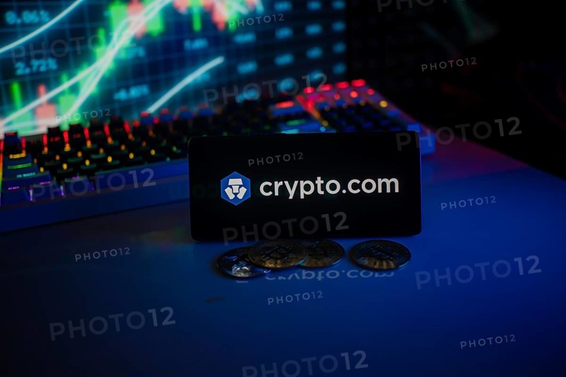 Phone displays Crypto.com logo with crypto coins and vibrant trading screen
